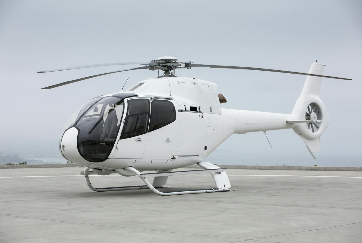 A Airbus H120 helicopter on a helipad, unmarked, seen from the front left