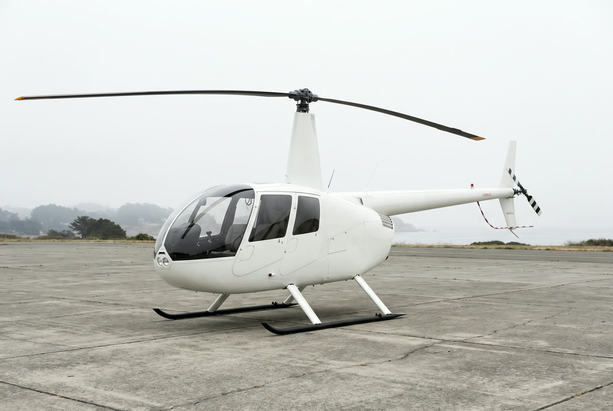 A Robinson R44 helicopter on a helipad, unmarked, seen from the front left